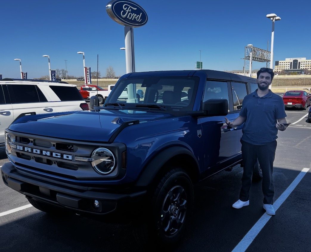 Customer standing beside a new dark blue Ford Bronco