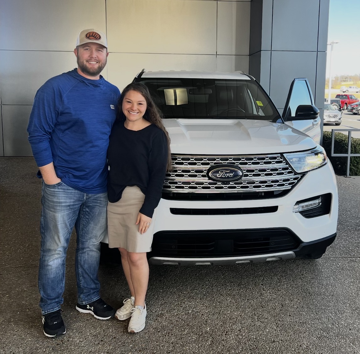 Couple posing with their new white Ford SUV at delivery