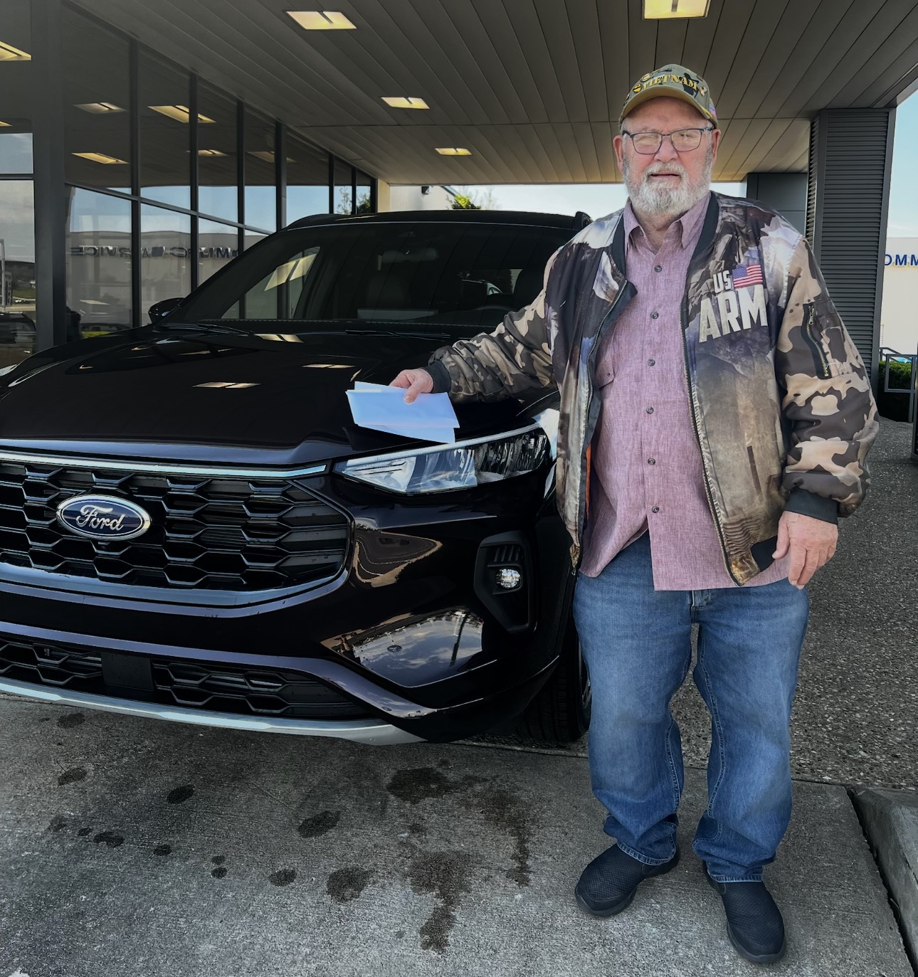 Veteran customer holding paperwork next to his new black Ford SUV