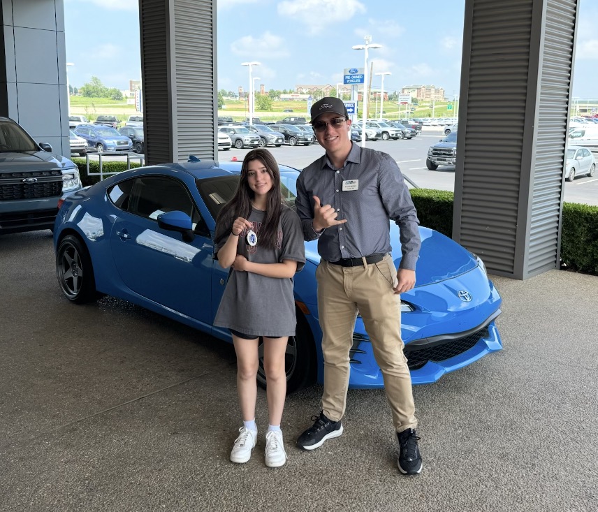 Customer holding up keys next to a bright blue sports car with Rylan Beebe
