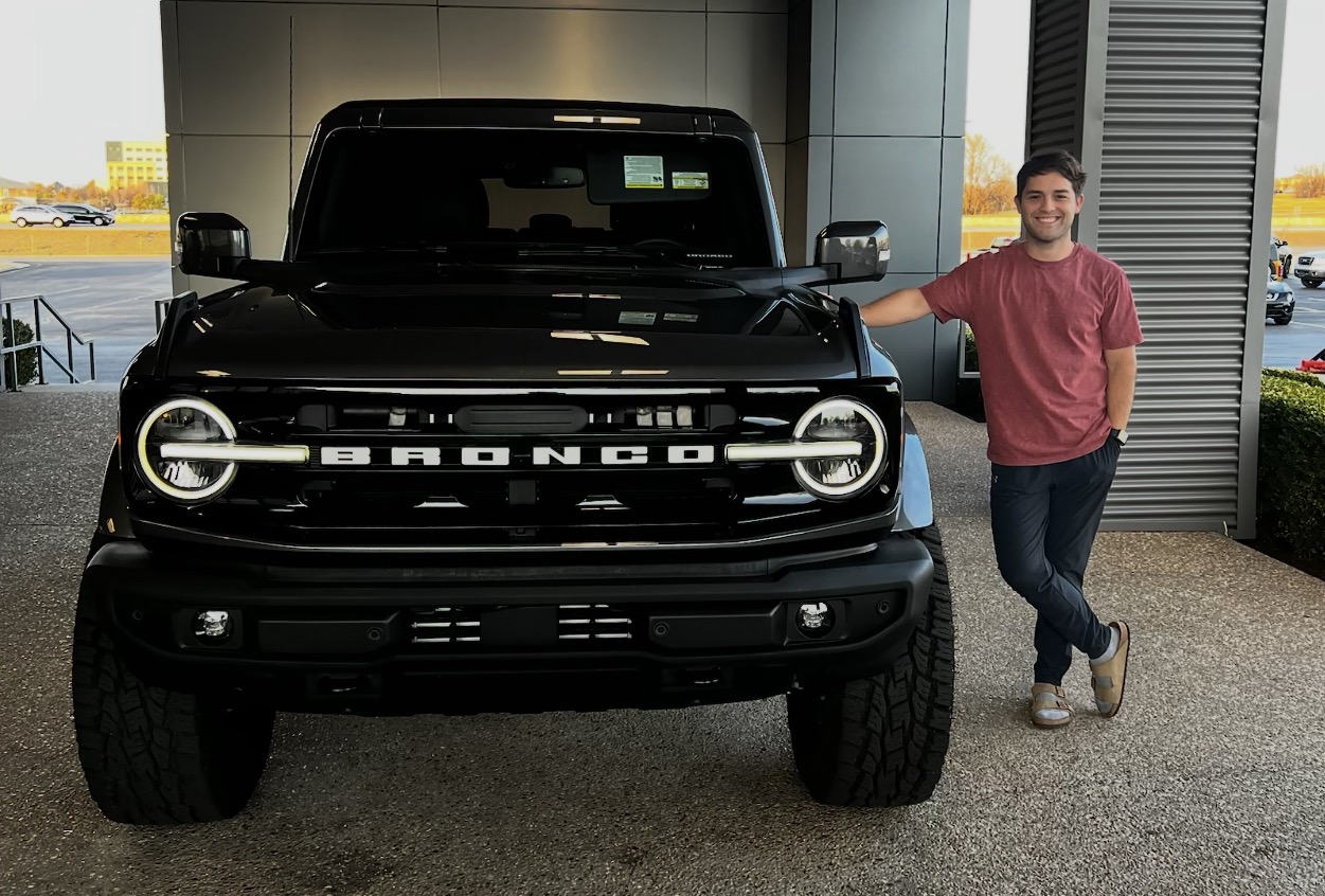 Smiling customer posing with his new black Ford Bronco
