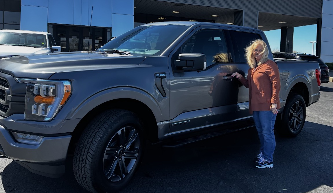 Customer beside a dark gray Ford F-150 PowerBoost at the dealership