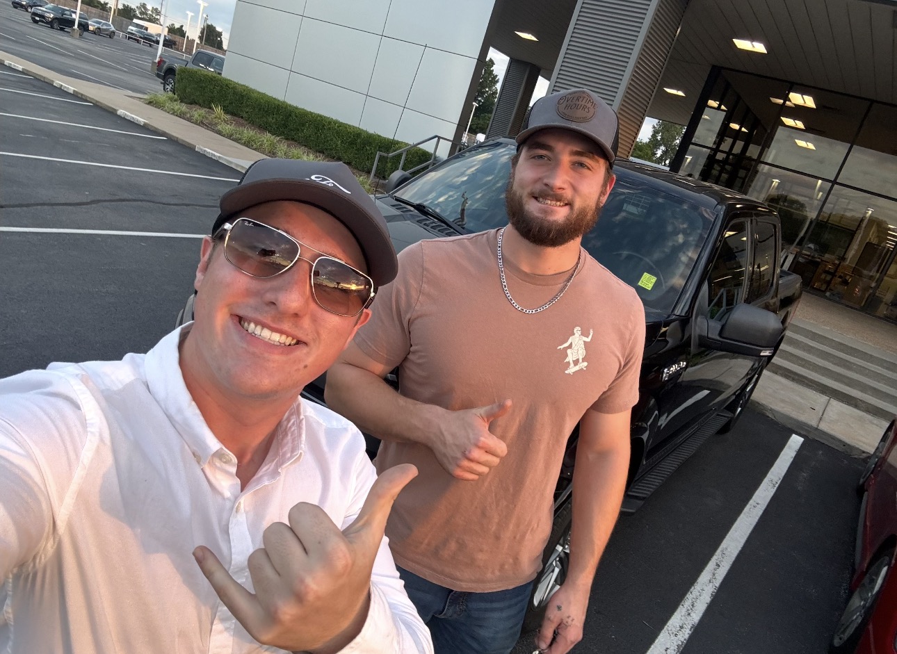 Two customers celebrating with shaka signs in front of a black pickup truck