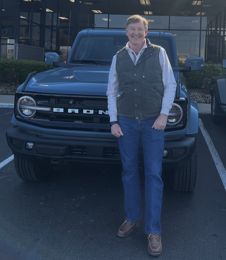 Smiling customer with a blue Ford Bronco at the dealership